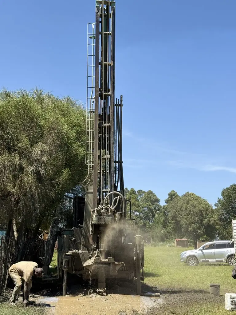 Drilling rig mast with water and cuttings at the borehole, Kaigat