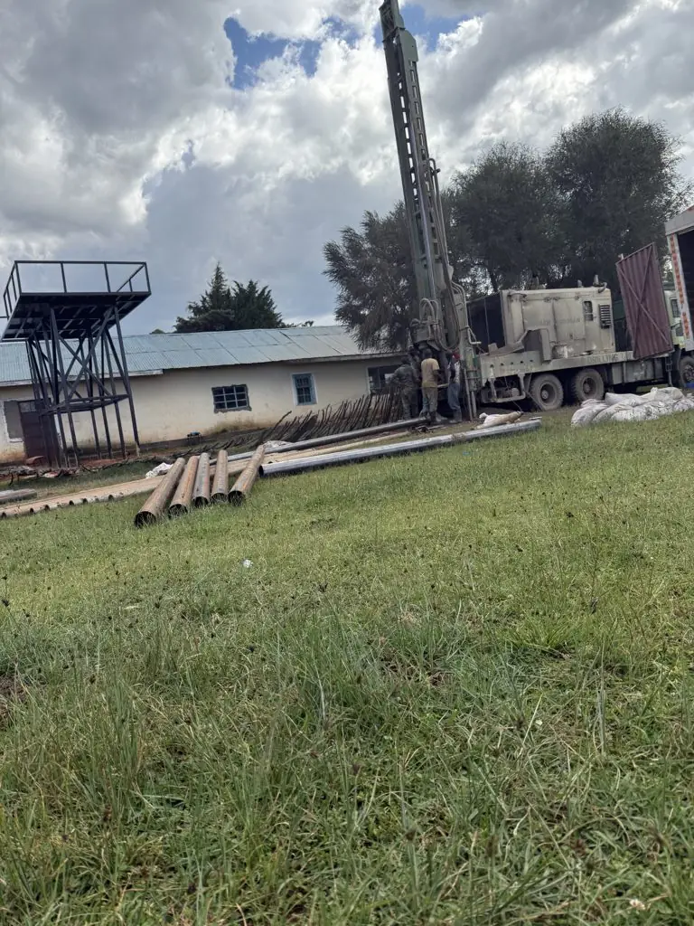 Rig, crew and casing pipes on the school grounds at Kaigat